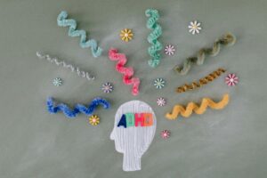 Illustration of a head silhouette labeled “ADHD” with colorful, wavy lines and flowers radiating from it on a gray background, symbolizing diverse thoughts.